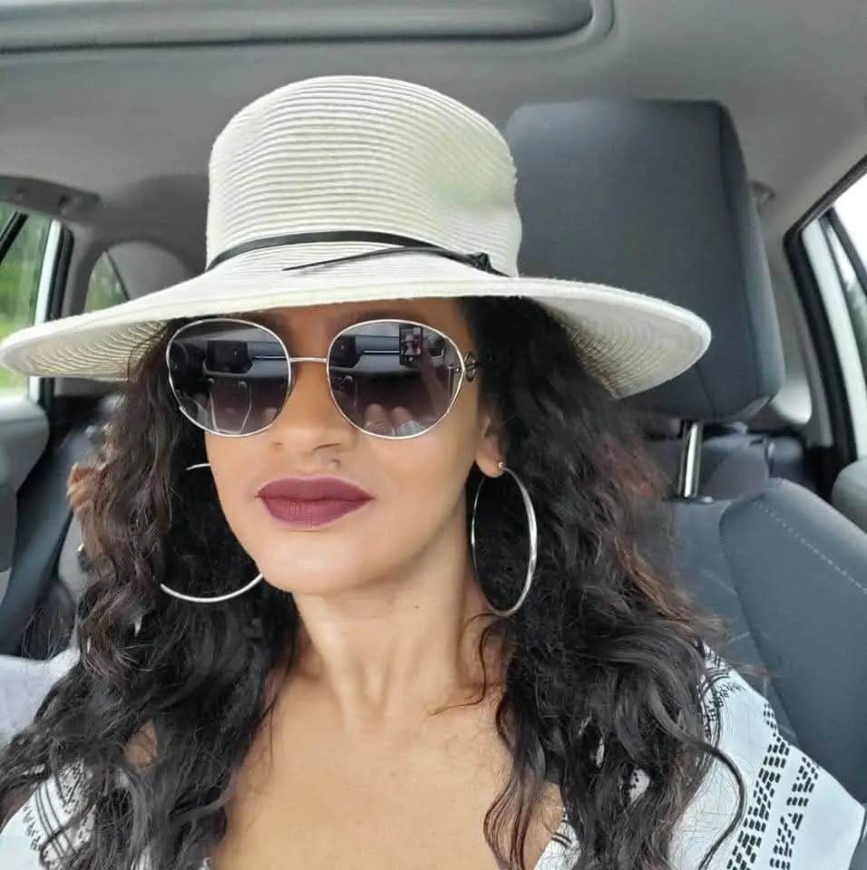 Addi with a sunhat and sunglasses looking at the camera, sitting in the car.