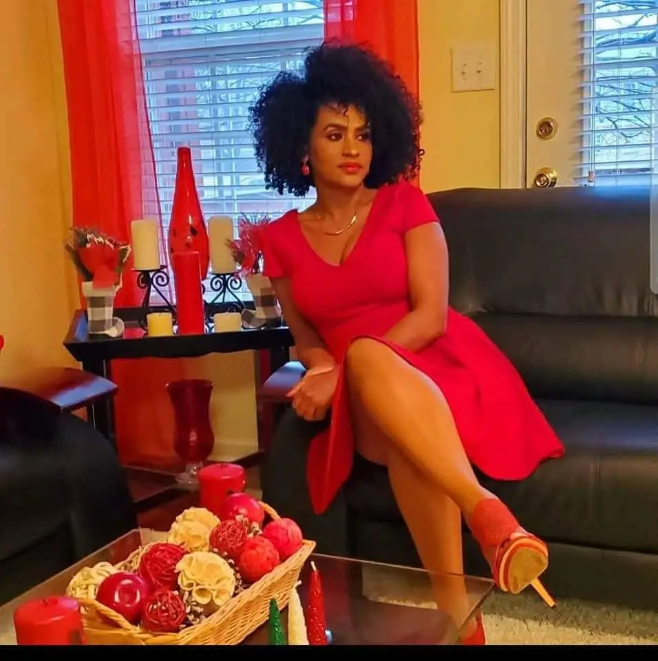 Addi profile picture in a red dress sitting on a black couch in a living room.